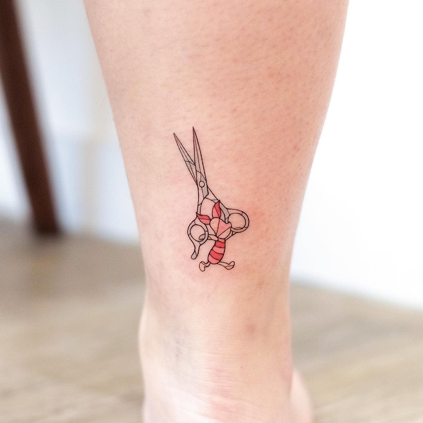 Tattoo of Piglet hanging from a pair of scissors on a person's leg